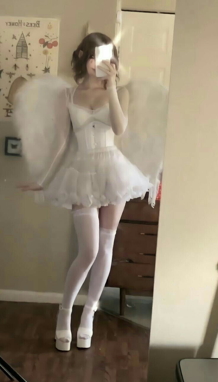 a woman taking a selfie in a white dress with angel wings on her head