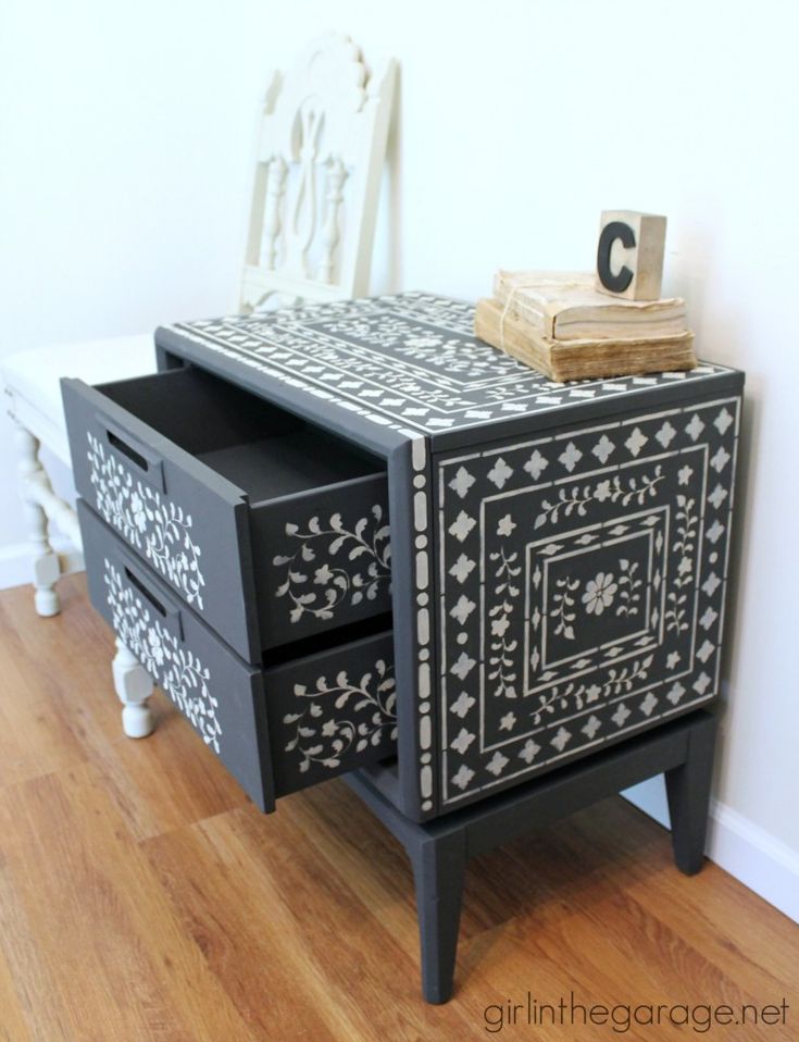 a black and white painted dresser next to a chair with a wooden block on top