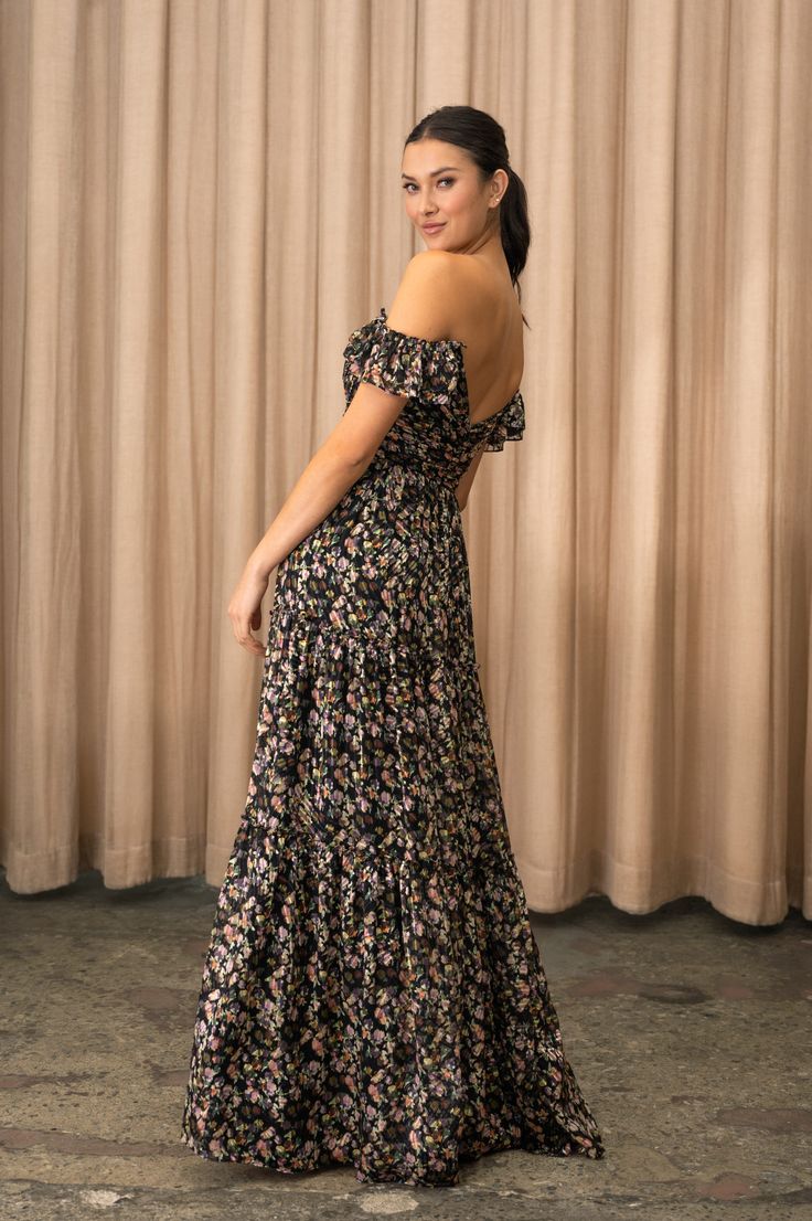 a woman standing in front of a curtain wearing a black and pink floral print dress