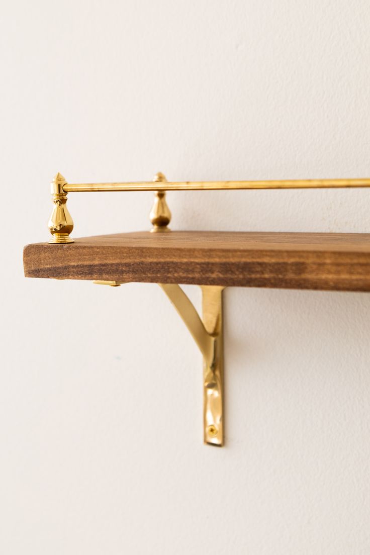 a wooden shelf with two brass hooks on it