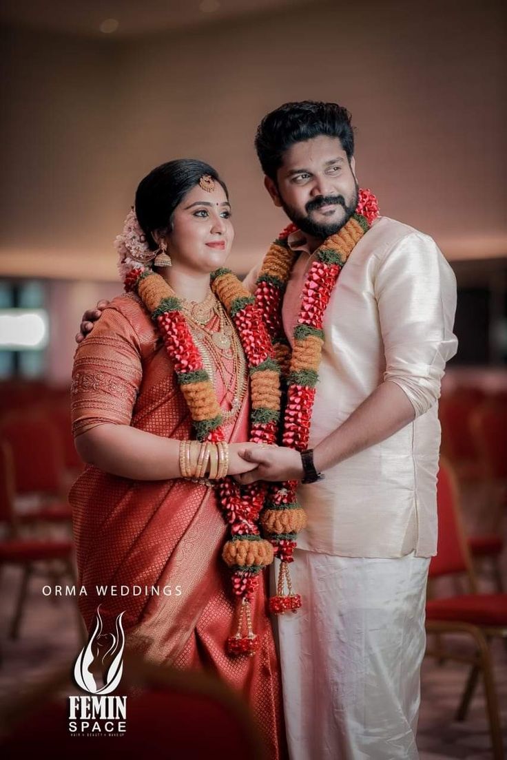 a man and woman standing next to each other in front of red chairs with garlands around their necks