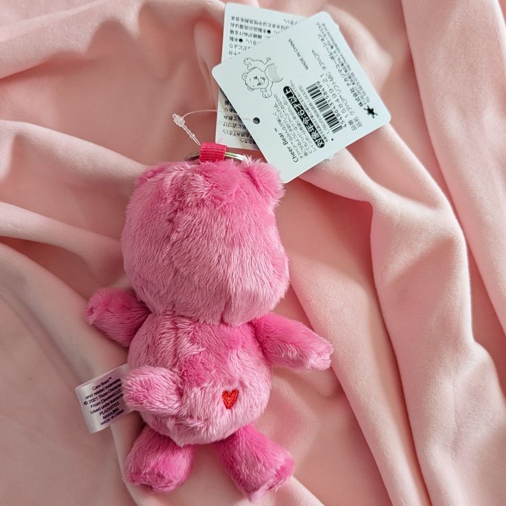 a pink teddy bear laying on top of a pink sheet with a tag attached to it