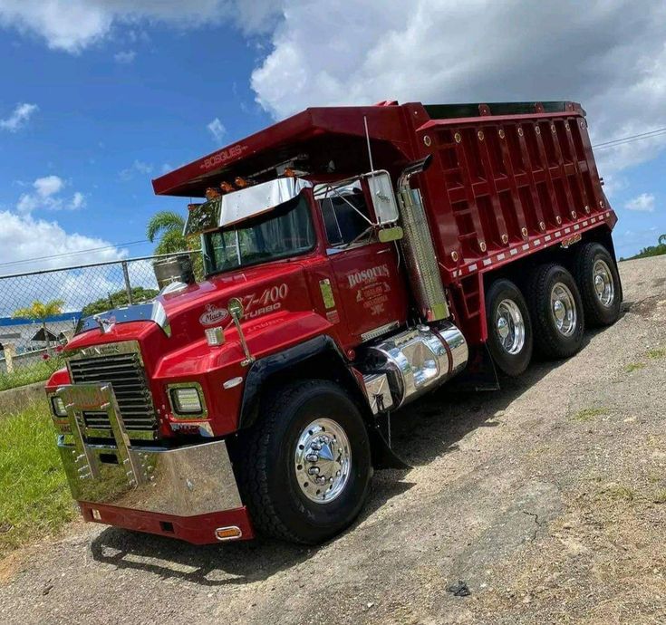 a red dump truck parked on the side of a dirt road next to a fence