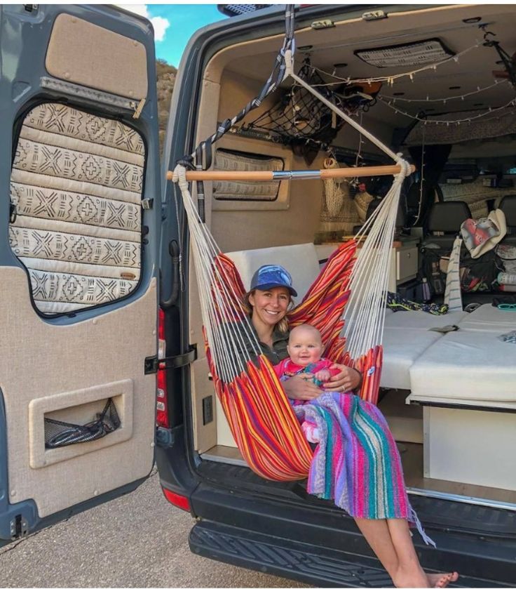 a woman holding a baby in a hammock next to an open van door