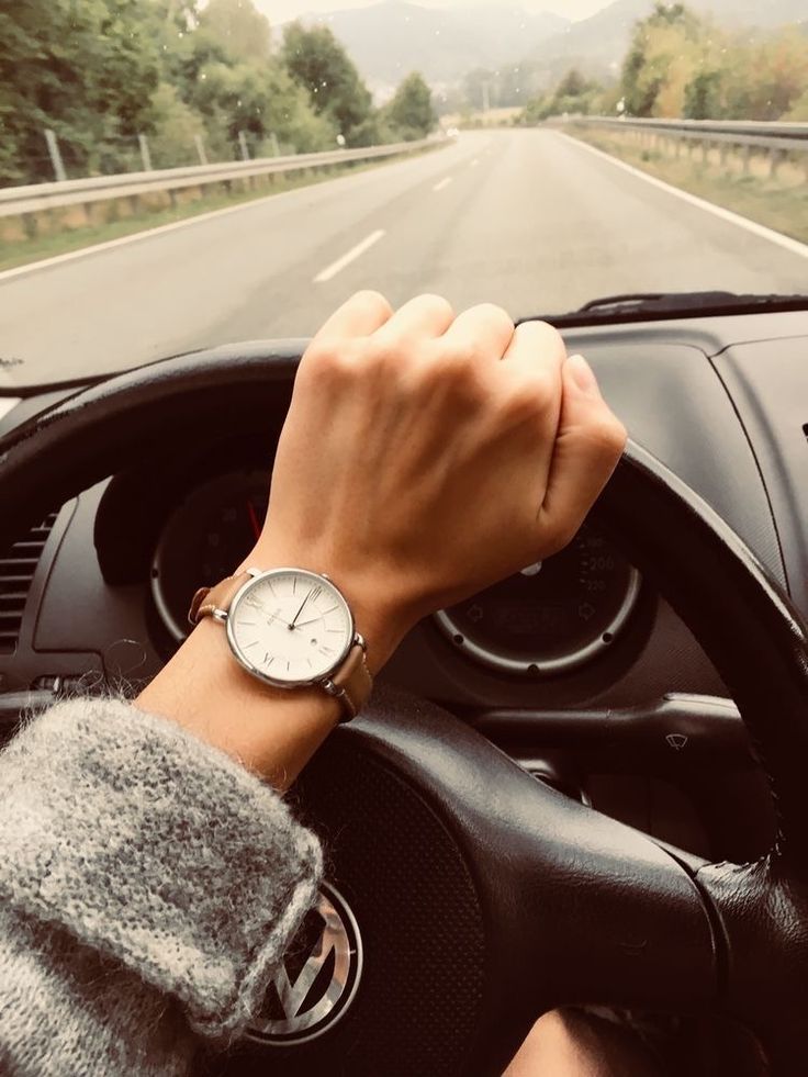 a person driving down the road with their hand on the steering wheel while wearing a watch