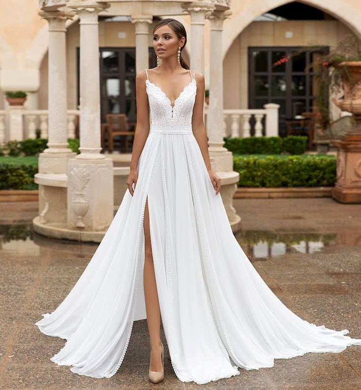 a woman standing in front of a building wearing a white dress with a slit down the side