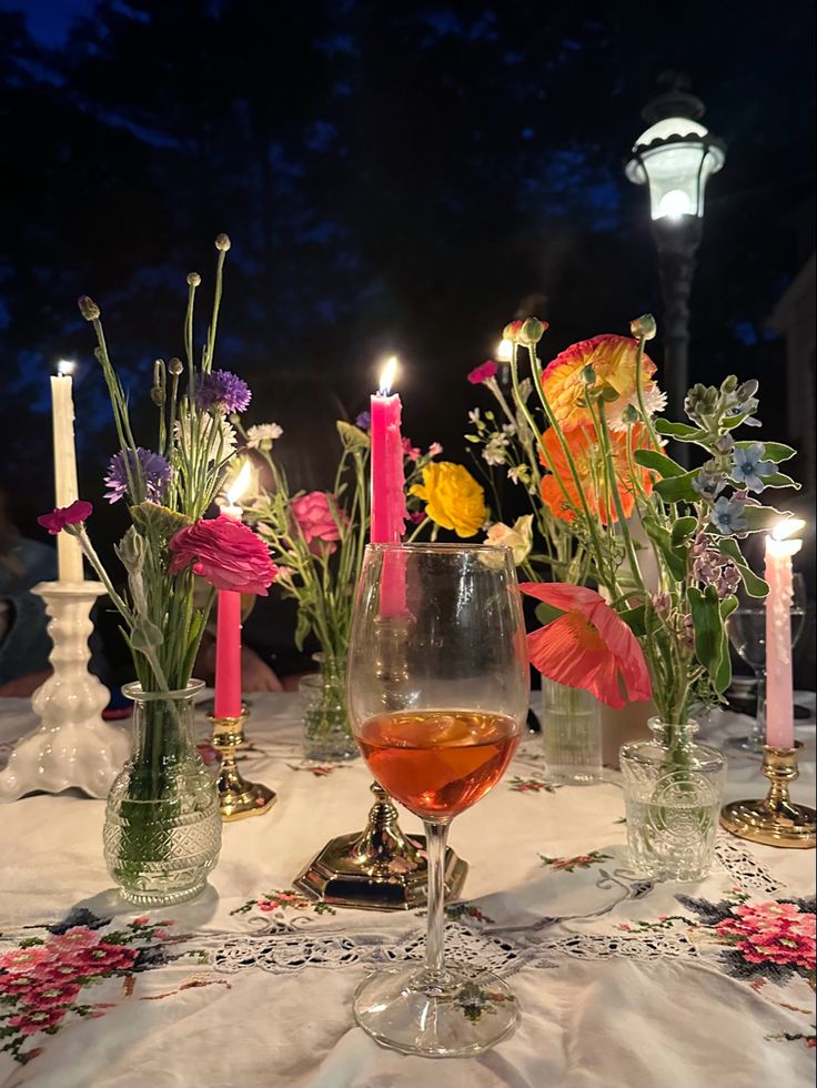 a table topped with glasses filled with liquid and flowers next to candles on top of a table