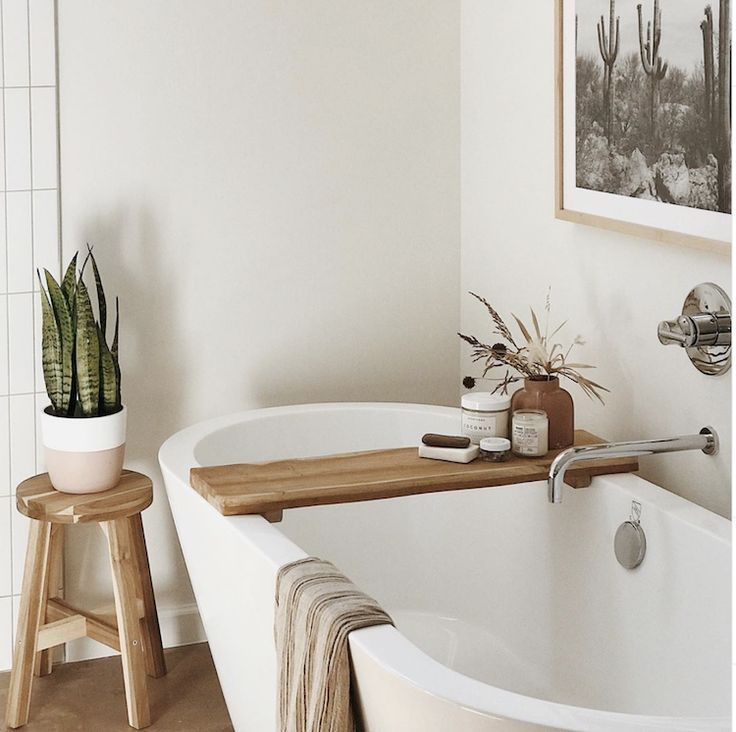 a white bath tub sitting in a bathroom next to a wooden stool and potted plant