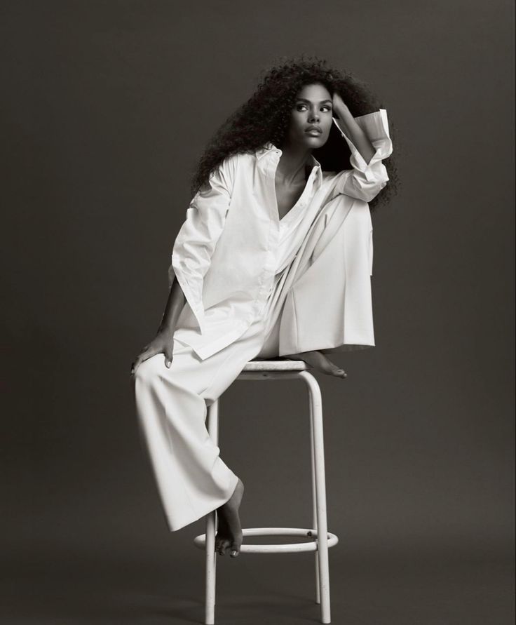 a woman sitting on top of a white chair wearing a white shirt and long pants