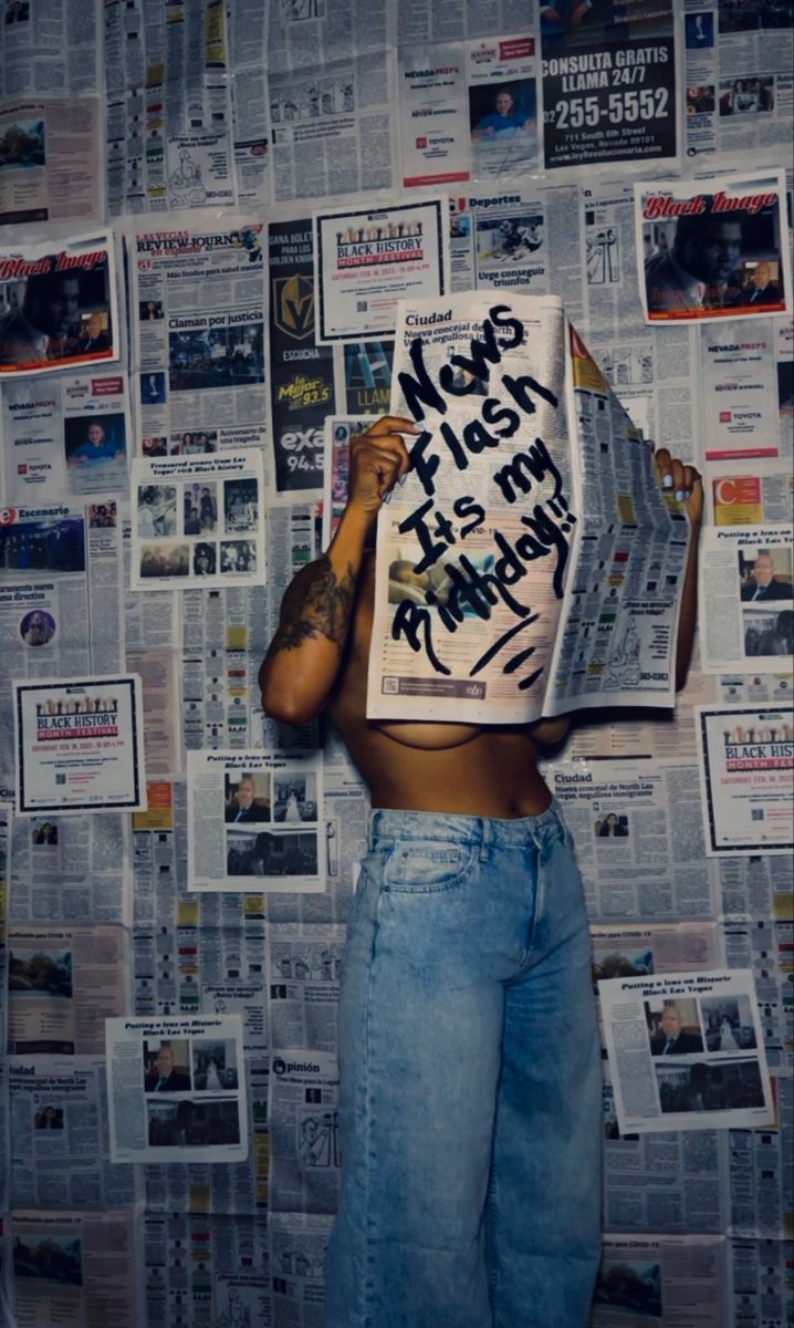 a woman holding up a news paper with writing on it in front of a wall full of newspapers