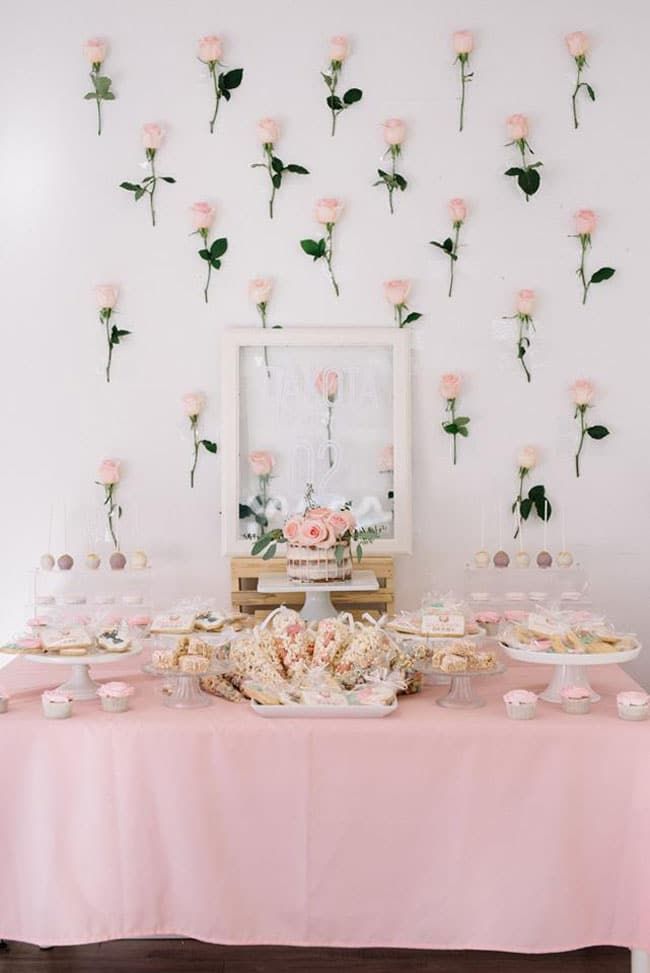 a table topped with lots of desserts and pink flowers on the wall behind it