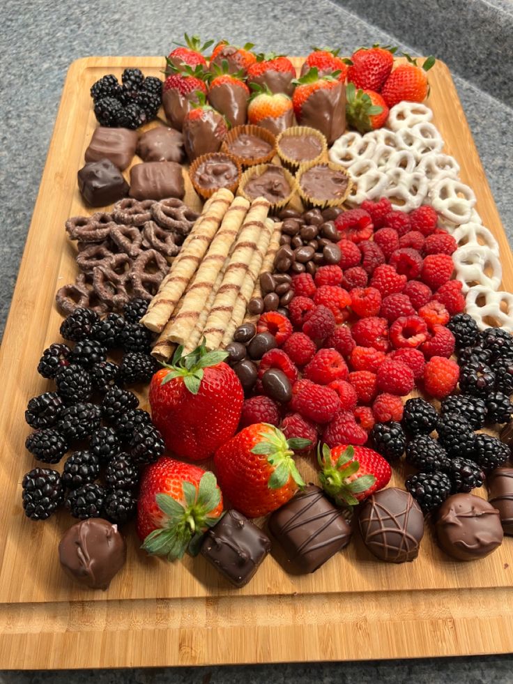 a wooden cutting board topped with lots of chocolate covered strawberries and other foods on top of it