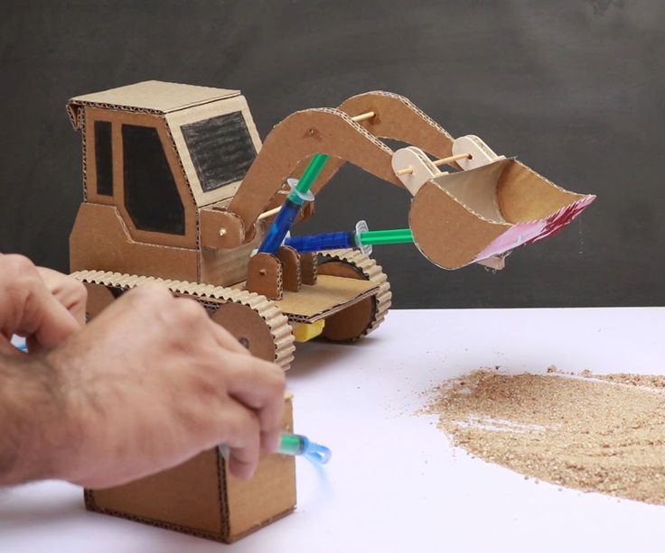 a cardboard construction vehicle is being made out of sand and paper with two men working on it