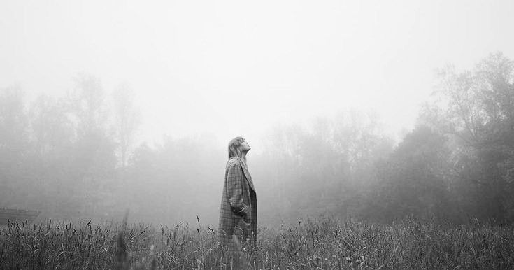 a man standing in the middle of a field on a foggy day