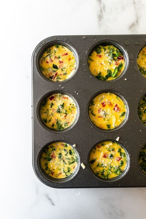 muffin tins filled with eggs and spinach on a marble countertop top