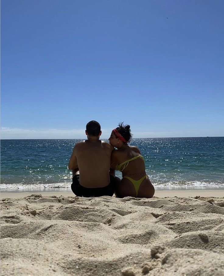 two people sitting in the sand at the beach