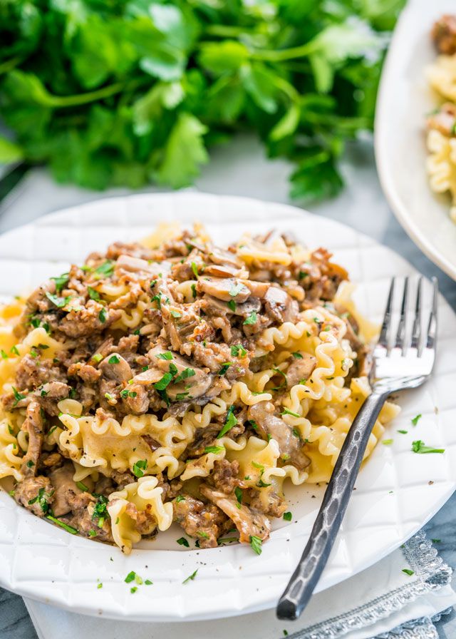 a plate of pasta with meat and parsley on the side next to a fork