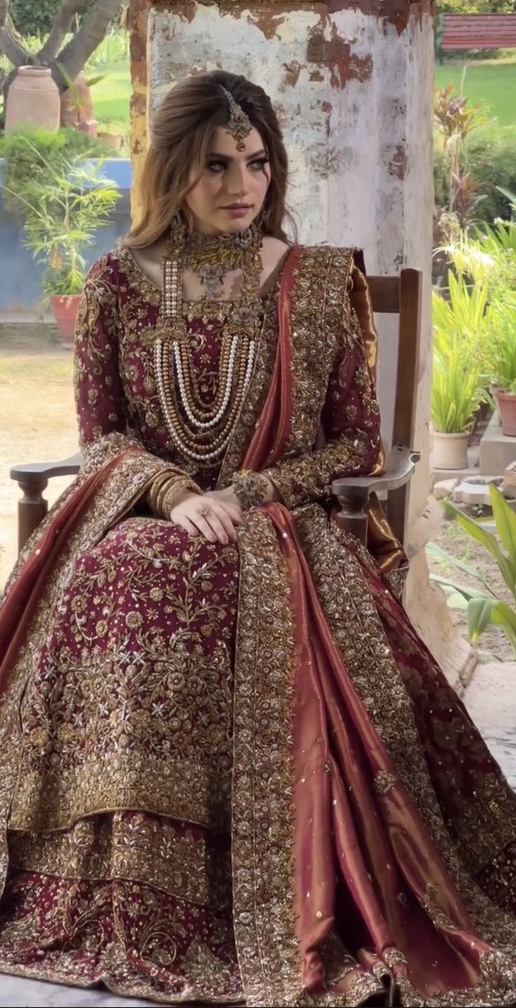 a woman sitting on top of a wooden chair wearing a red and gold dress with an elaborate