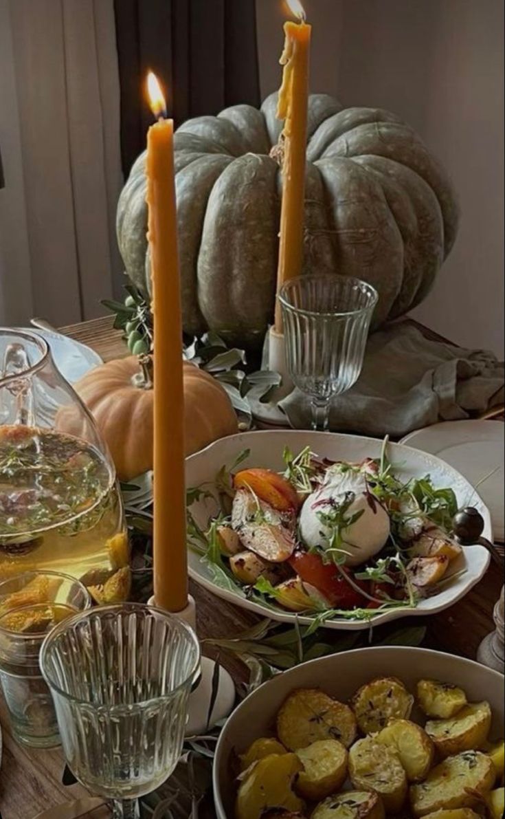 a table topped with plates and bowls filled with food next to two lit candles on top of each plate