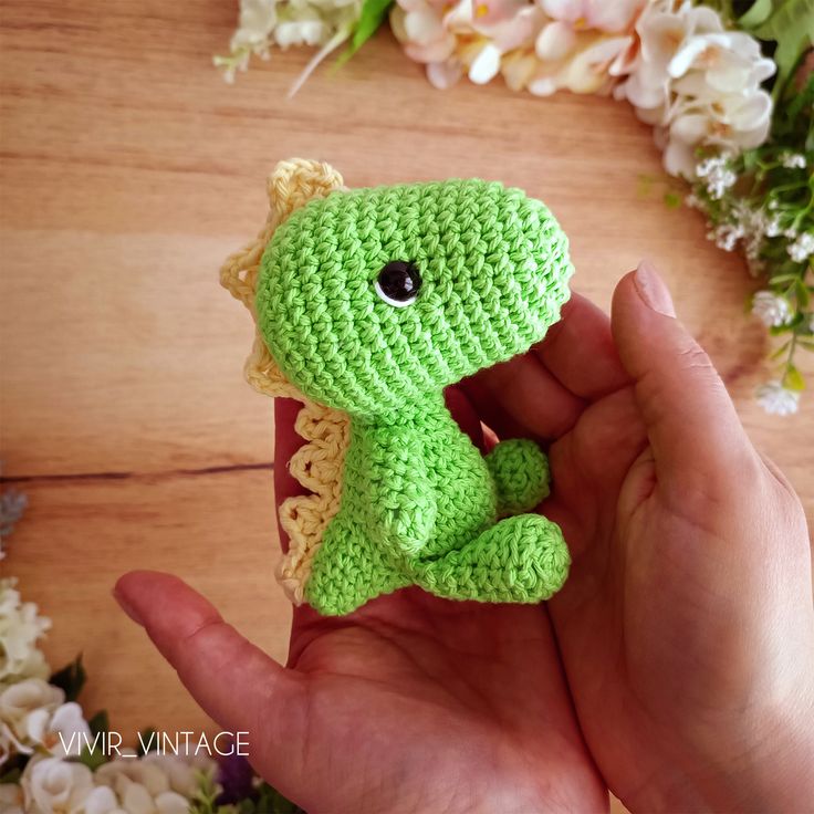 a small crocheted green toy sitting on top of a wooden table next to flowers