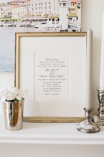 a white mantle with a framed photograph and flowers on it next to two silver candles