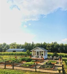 a small white house sitting in the middle of a lush green field next to a wooden fence