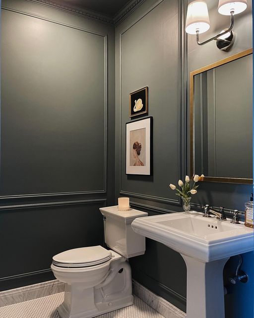 a white toilet sitting next to a sink in a bathroom under two lights on the wall