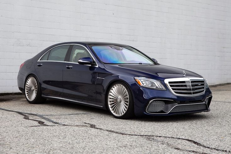 a blue mercedes s - class parked in front of a white brick wall with chrome rims