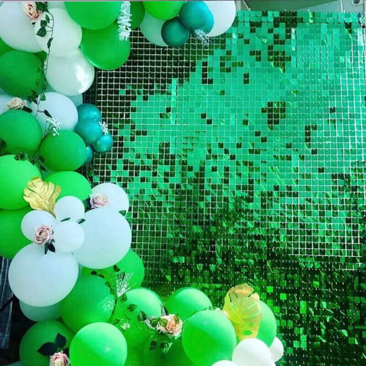 green and white balloons are hanging from the ceiling in front of a mosaic wall with flowers