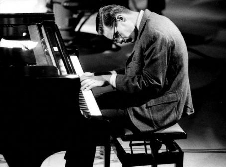 a man sitting at a piano with his hands on the keyboard and looking down as he plays it