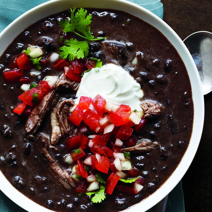 a white bowl filled with black bean soup and topped with sour cream