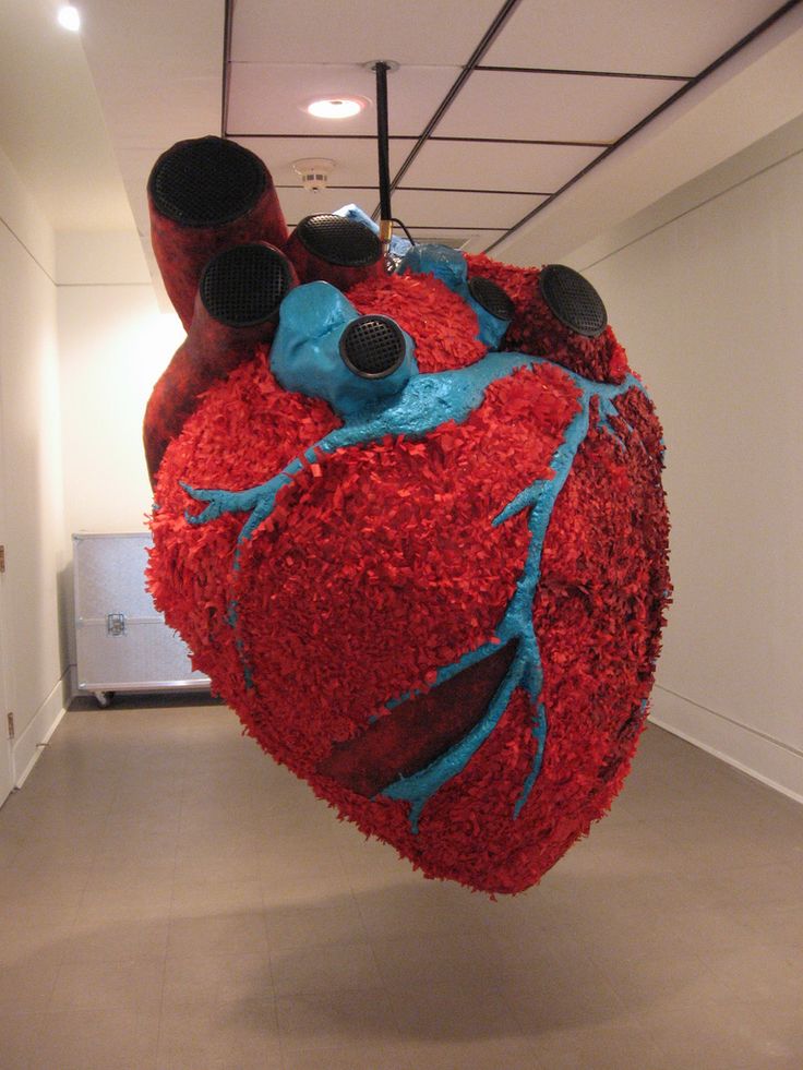 a heart shaped sculpture made out of red and blue flowers in an office hallway with pipes on the ceiling