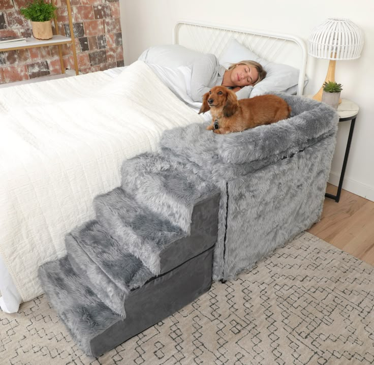 a woman laying in bed with her dog on top of the stairs that lead up to the bed