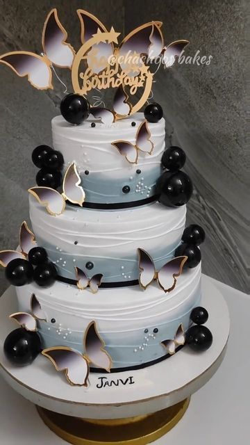 a three tiered wedding cake with black and white butterflies on the top, sitting on a gold pedestal