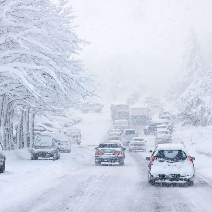 cars driving down a snow covered road in the middle of winter, with trees on both sides