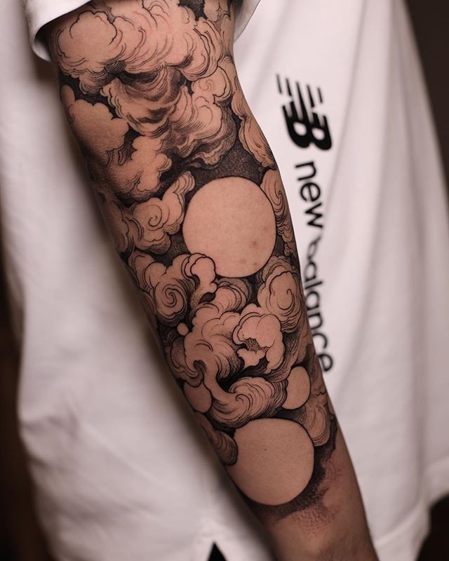 a man's arm with clouds and sun tattoo on his left arm, in black and white