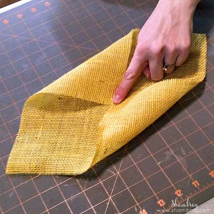 a person using a yellow cloth to clean a piece of fabric on a cutting board