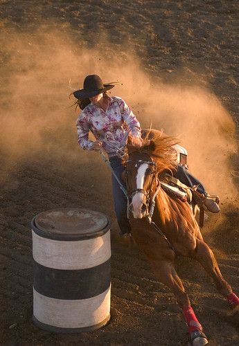 a woman riding on the back of a brown horse next to a white barrel in an arena