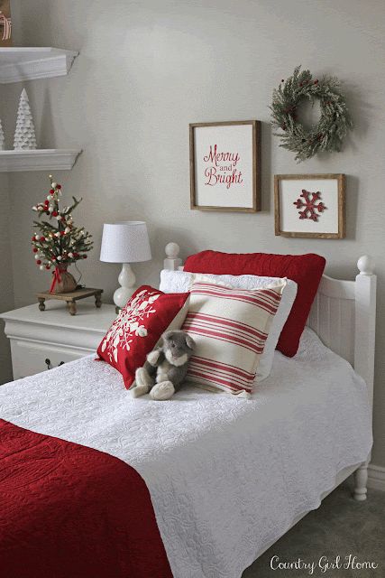 a white bed topped with red pillows next to two christmas wreaths on the wall