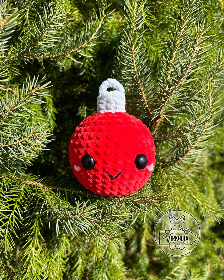 a knitted ornament hanging from a pine tree in the shape of a red ball