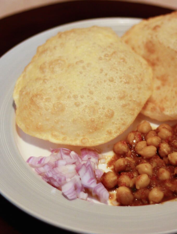 a white plate topped with bread and beans next to red onion on a wooden table