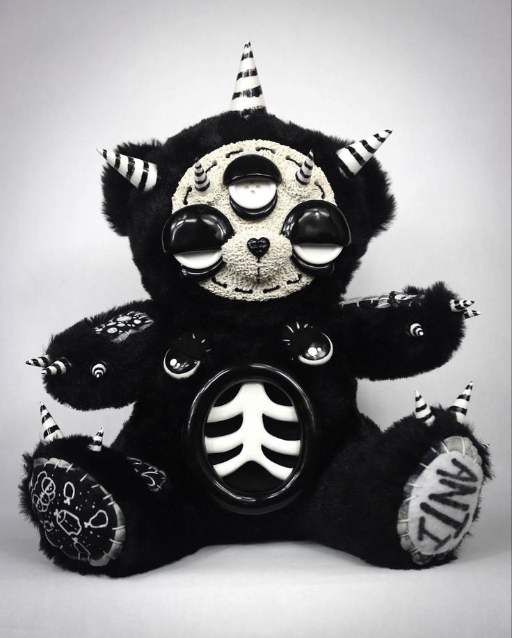 a black teddy bear with white and black decorations on it's face, sitting in front of a gray background