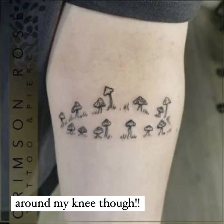 a person with a tattoo on their leg that has mushrooms all over it and trees in the background