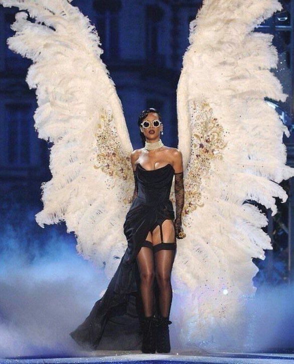 a model walks down the runway in a black dress with large white feathers on her wings