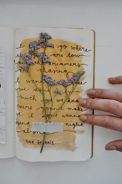 a hand holding an open book with writing on it and flowers in the pages next to each other