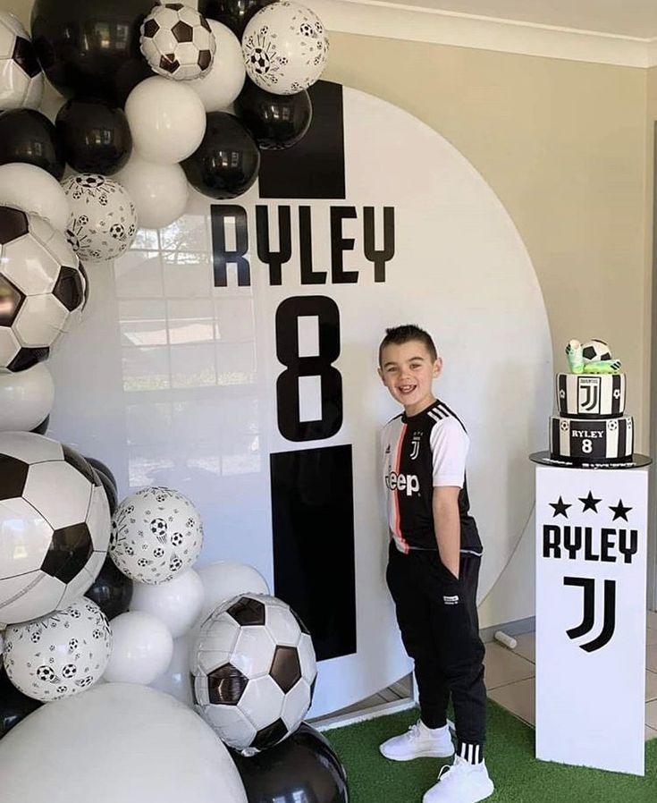 a young boy standing in front of a wall with soccer balls on it's sides