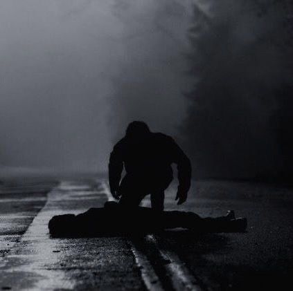 a person kneeling down on the side of a road in the dark with fog behind them