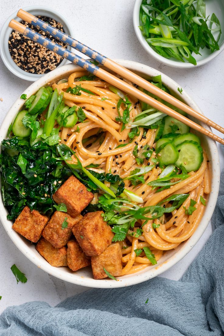 a bowl filled with noodles and vegetables next to chopsticks on top of a table