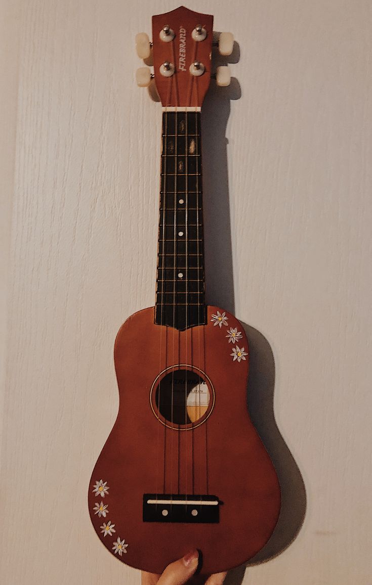 a person is holding an ukulele in front of a white wall with flowers on it