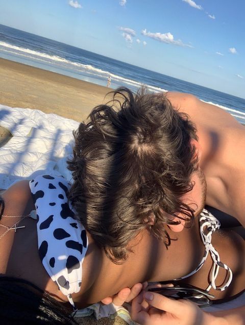 a man laying on top of a beach next to the ocean holding a cell phone